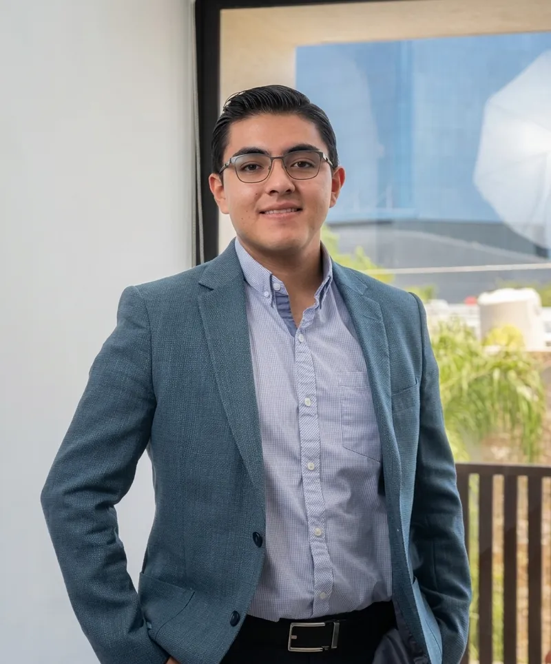 David de pie en una oficina, con saco azul y camisa a cuadros, sonriendo